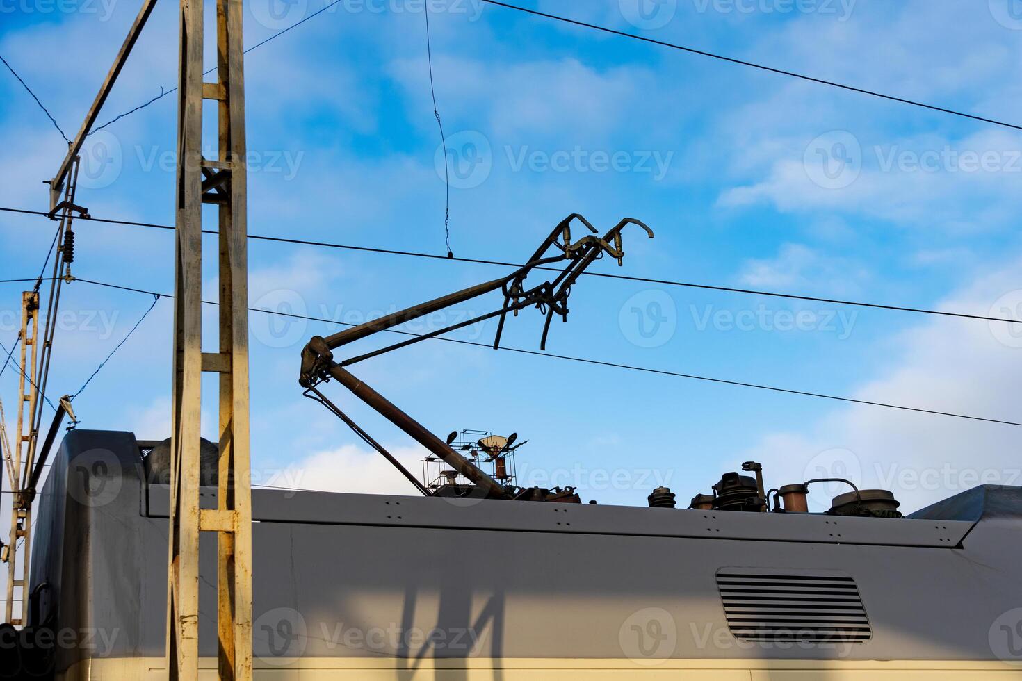 An electric train operates efficiently under clear blue skies, with its pantograph extended to connect with overhead supply lines. This showcases the advancement in railway technology photo