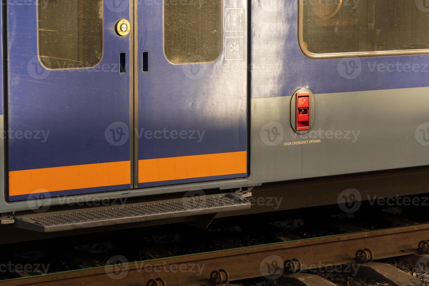 The sleek design of modern electric train doors stands out at a railway station, illuminated by warm light from the setting sun. Trains await passengers on the platform photo