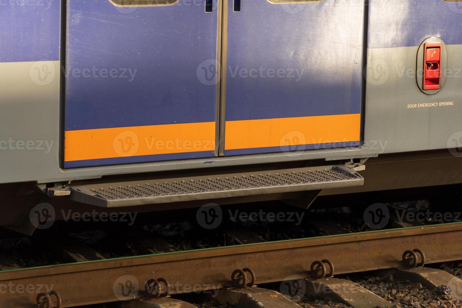 A modern electric train stands at a railway platform, showcasing its closed doors. Nearby, the tracks undergo maintenance during the late afternoon, highlighting industrial efficiency photo