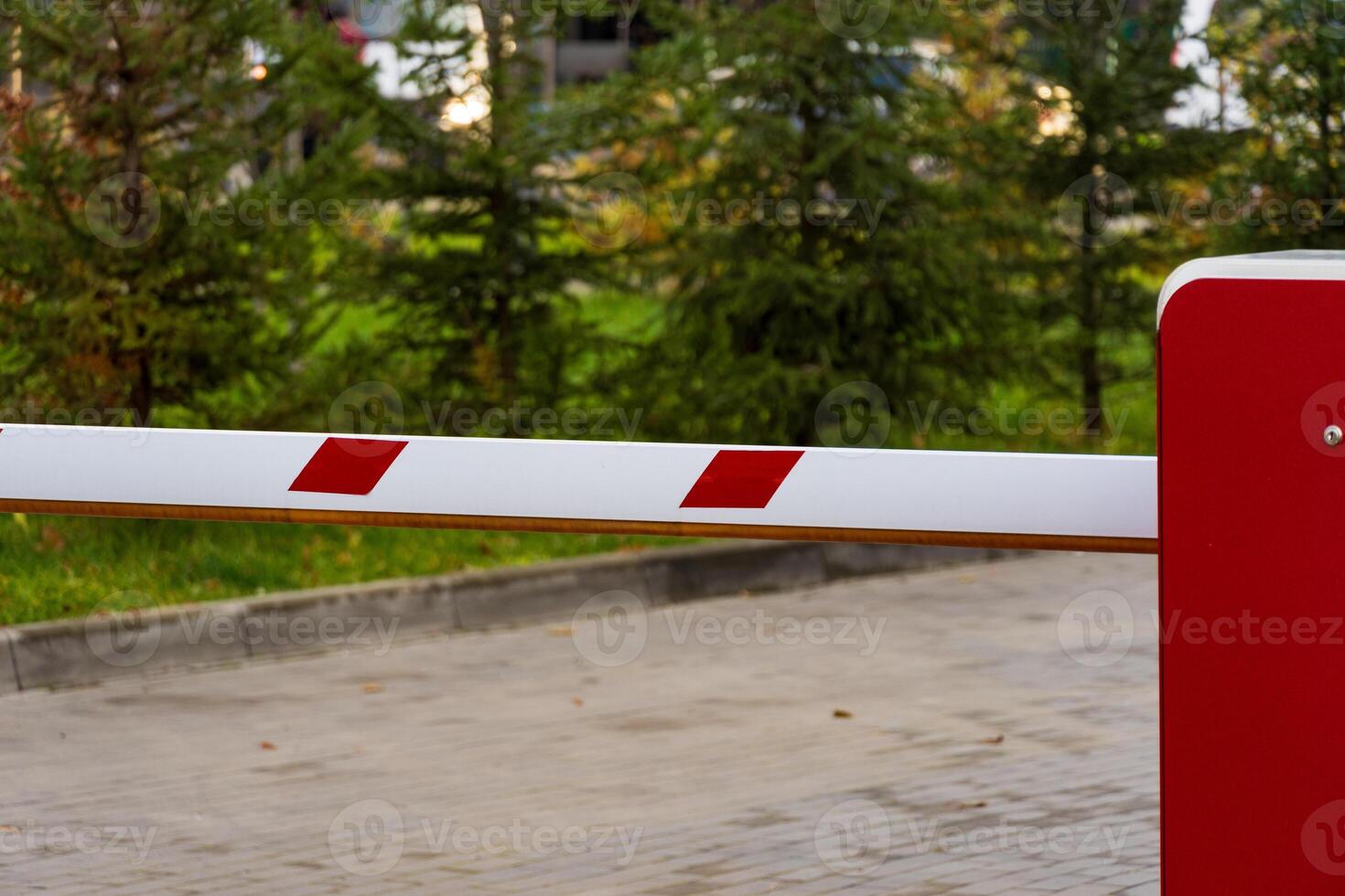 A barrier gate stands closed at the entrance to a parking lot, preventing unauthorized access. The surrounding area features greenery, emphasizing the need for security in this location photo