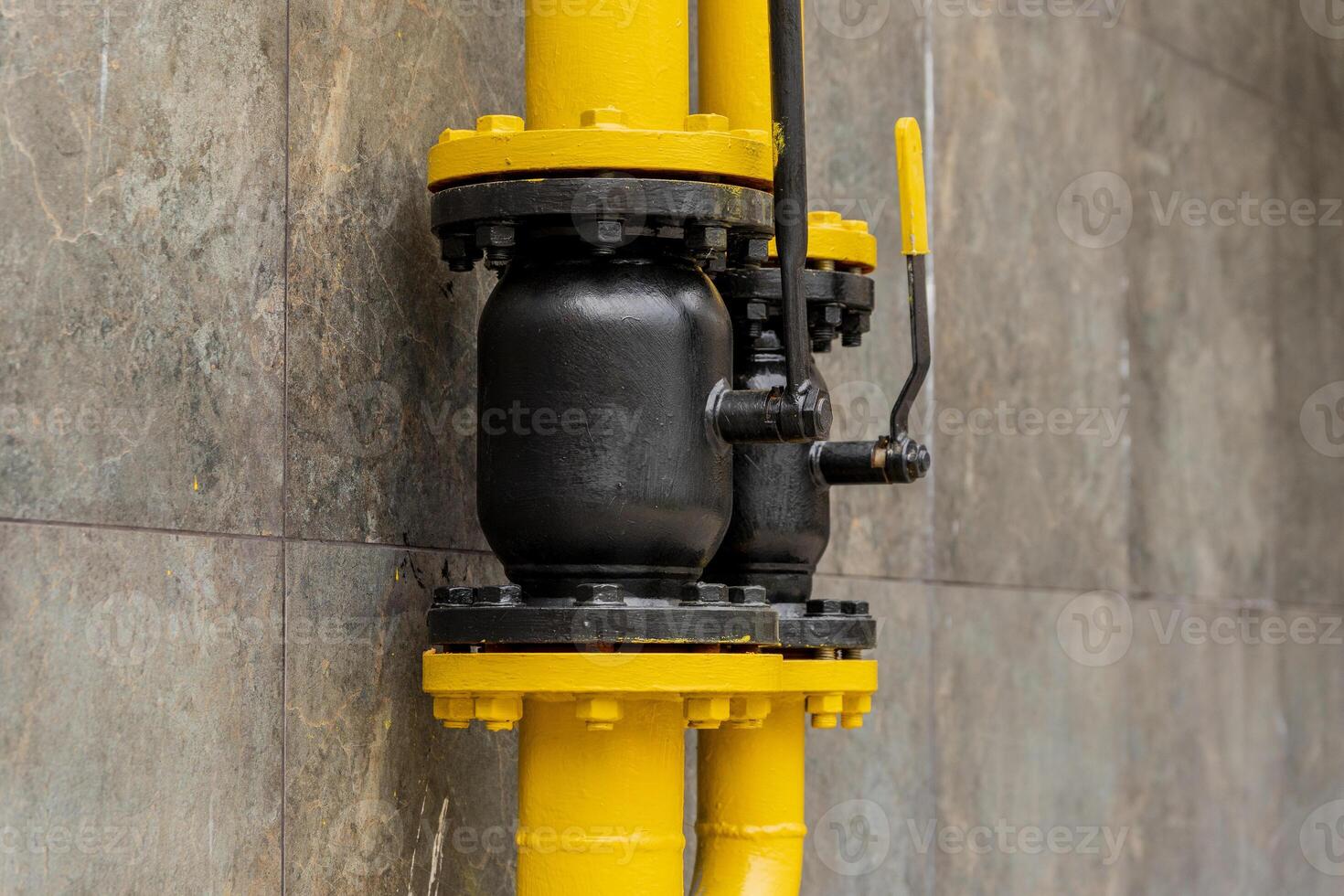 A yellow gas pipe with a black valve is mounted on a grey wall, showcasing an essential connection for transporting gas. The setup reflects modern energy infrastructure photo