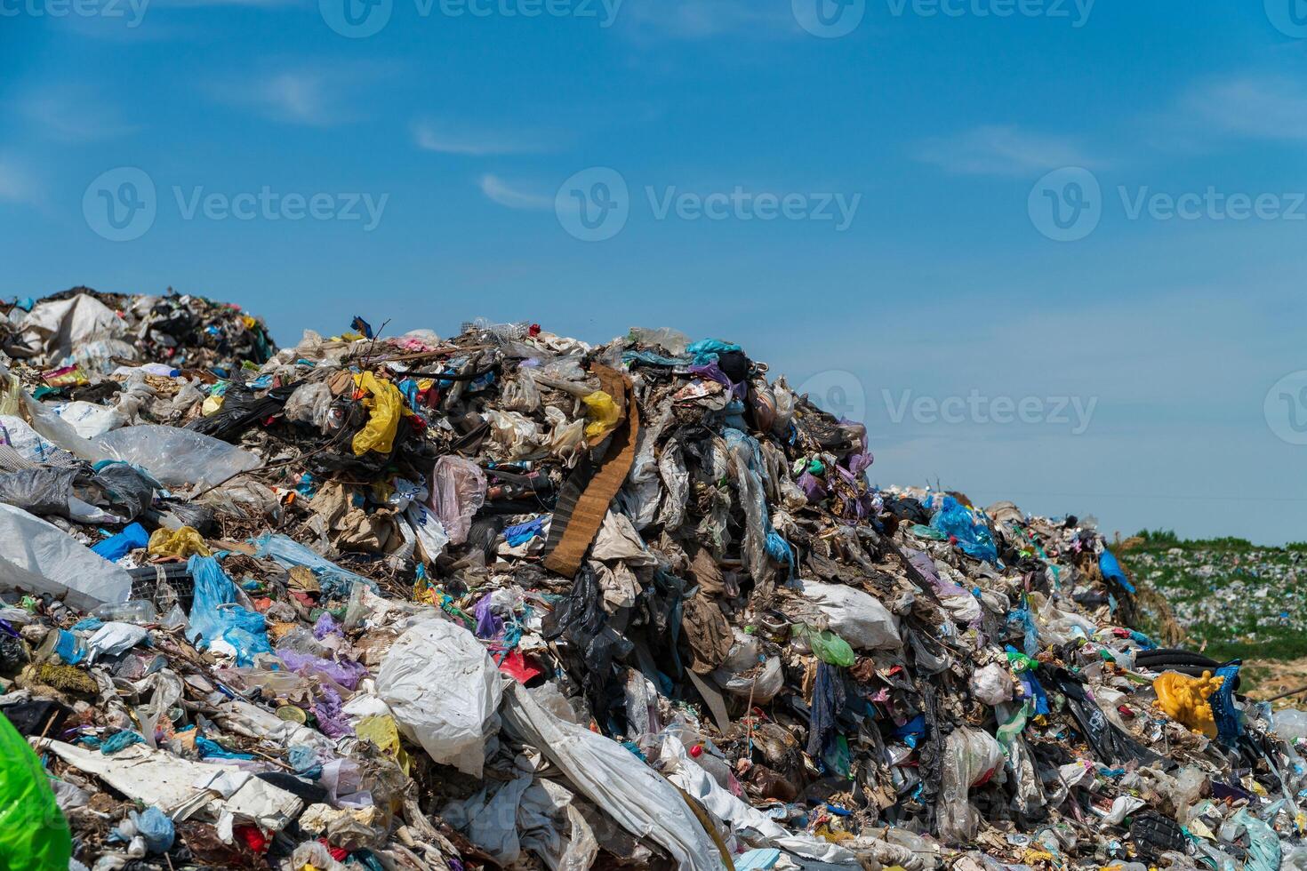 A towering pile of garbage filled with plastic and debris dominates the landscape under a clear blue sky, reflecting the serious issues of pollution and waste management in the environment photo