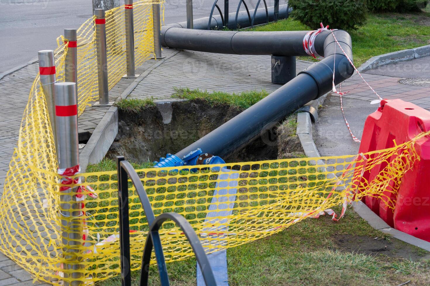 Workers are replacing old water pipes on the street, using digging equipment while ensuring safety with barriers and caution tape around the construction site photo