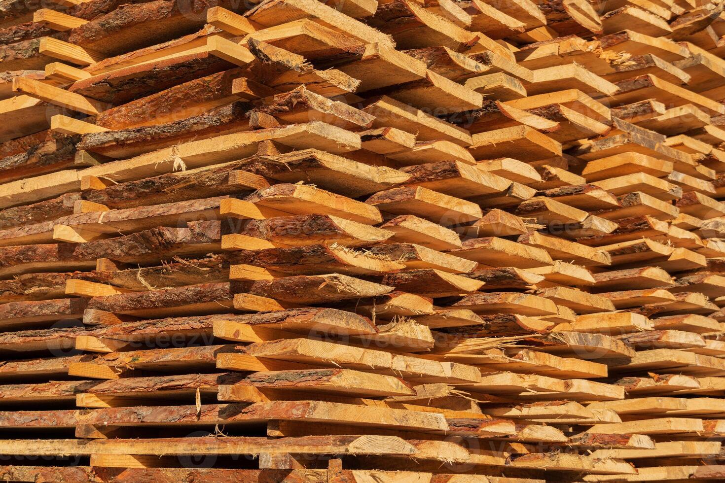 Sunlight filters through wooden stacks at a sawmill, revealing freshly cut timber planks arranged neatly. The warm tones of the wood highlight the texture, showcasing quality lumber photo