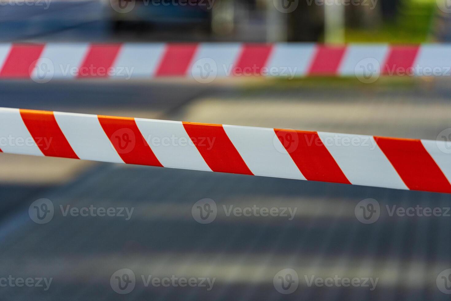 Caution tape with bright red and white stripes is stretched across a pathway in a city, indicating a warning and restricting access to a certain area during the day photo