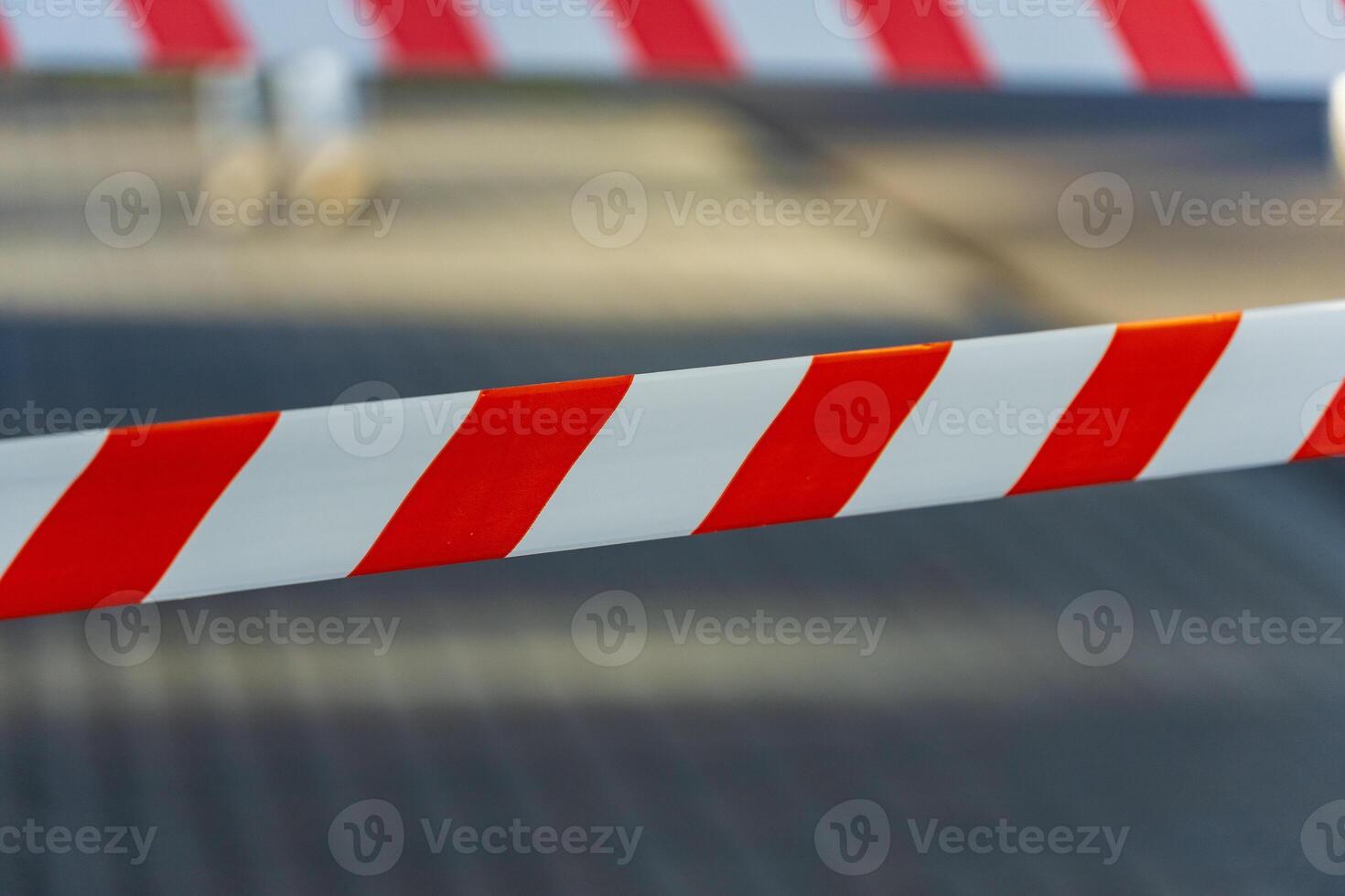 Bright red and white caution tape spans across a designated area in a city, signaling danger and restrictions. The tape serves as a clear warning to pedestrians and vehicles photo