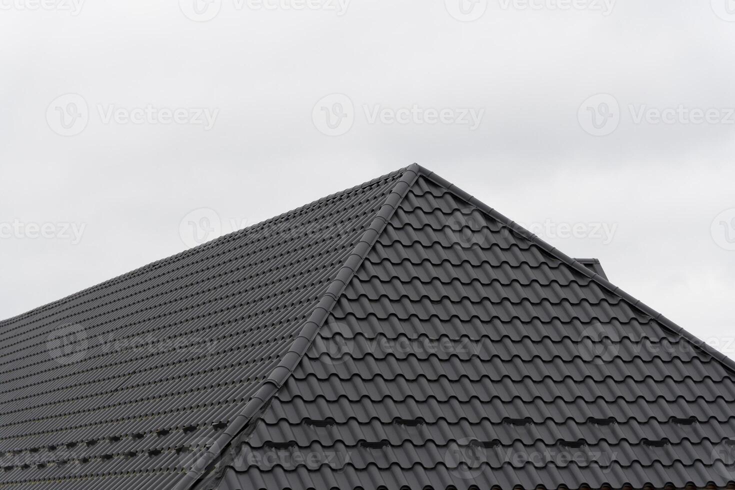 A sleek modern rooftop covered with metallic tiles complements the architecture of a residential house. The setting features an overcast sky, enhancing the contemporary design photo