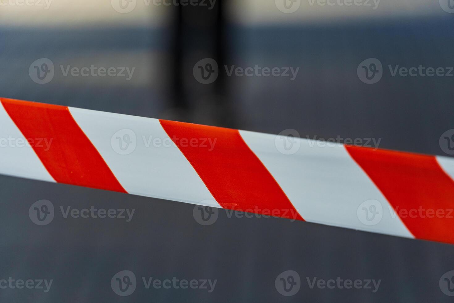 Bright red and white caution tape marks a restricted area in an urban setting, signaling danger and the need for caution. People are visible in the background, emphasizing city life photo