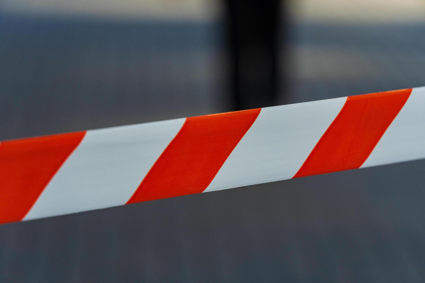 Bright red and white caution tape wraps across the city pavement, serving as a barrier. Its vivid colors stand out under a clear sky, guiding passersby away from a restricted area photo