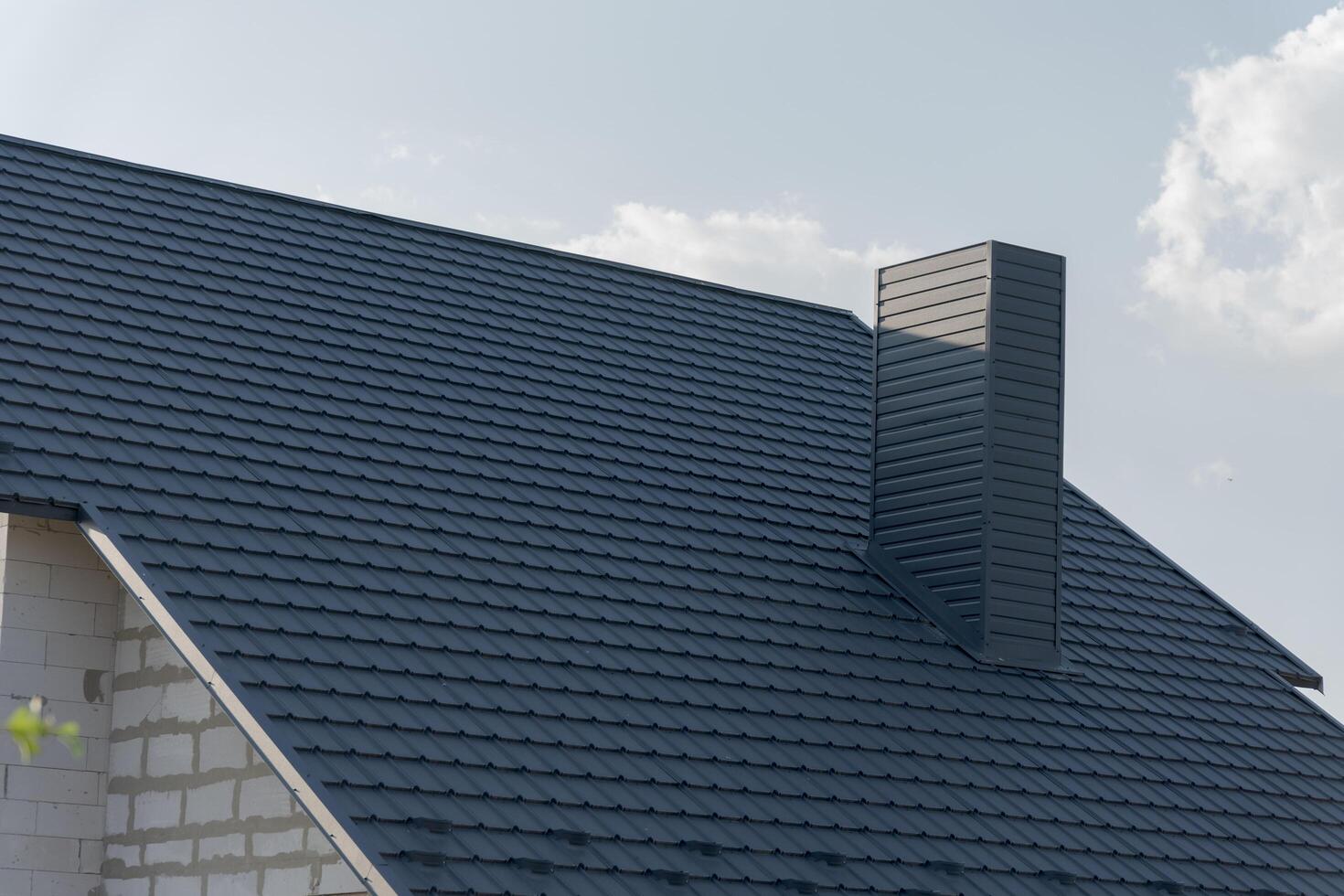 A beautiful modern house boasts a stylish dark slate roof, highlighting the clean lines and architectural design. Sunlight reflects off the roof shingles as clouds drift lazily photo