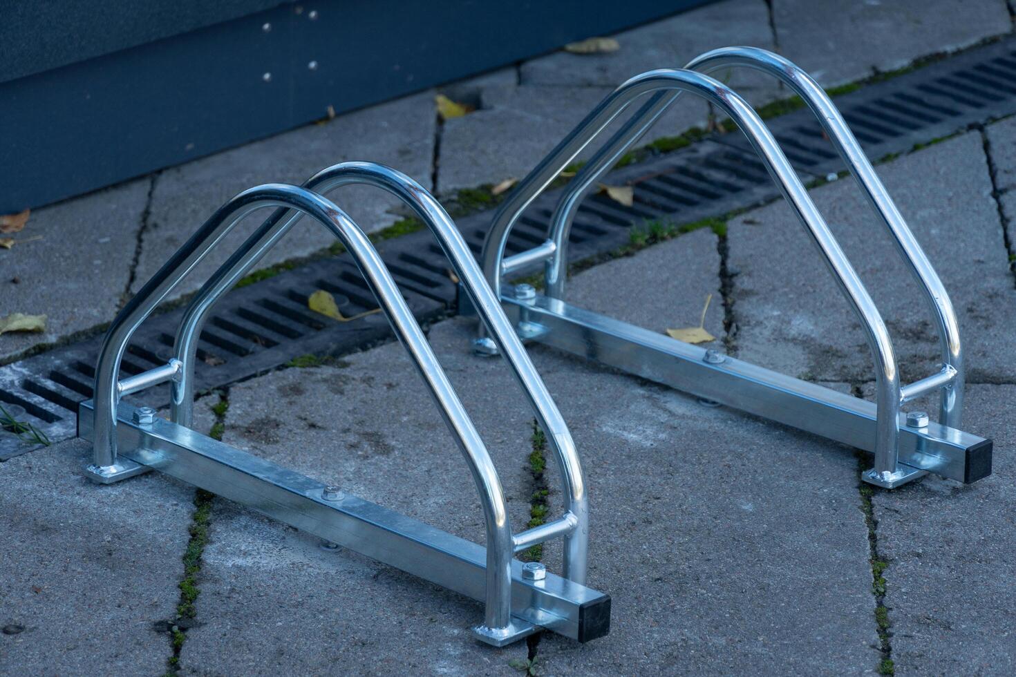 Two sleek and sturdy bicycle racks are positioned on a clean concrete sidewalk. Leaves are scattered nearby, hinting at the changing seasons and adding a touch of nature to the urban setting photo