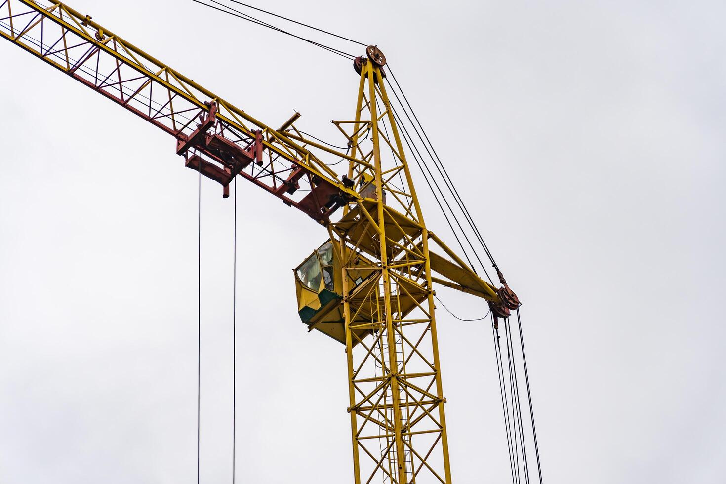 A tall yellow crane stands prominently against a gray sky, while workers maneuver materials at a construction site, showcasing urban development and labor in action photo