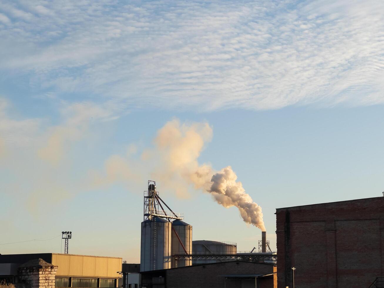 Amidst the golden hour, towering smokestacks billow steam into the atmosphere, blending industrial activity with tranquil evening skies, creating a striking contrast photo