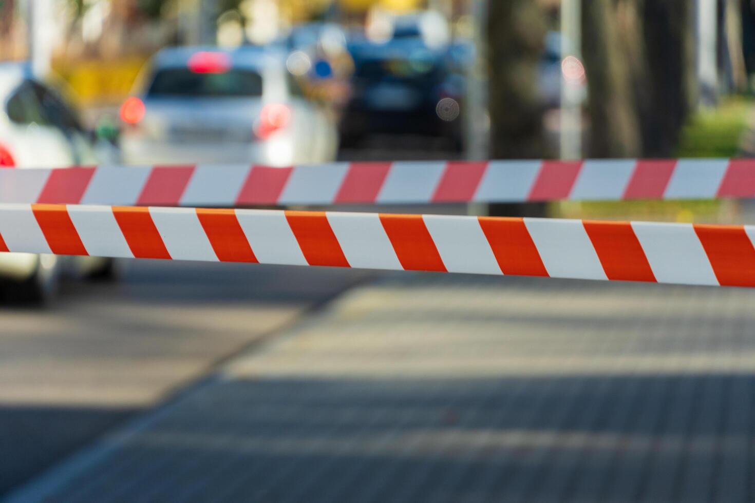 A vivid scene captures a barrier with distinct red and white stripes, preventing entry to a busy street filled with parked cars and blurred city life beyond photo