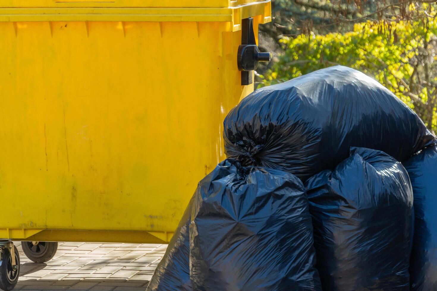 A yellow garbage can stands prominently in a lively urban area, surrounded by neatly piled black garbage bags, showcasing the essence of city life and waste management photo
