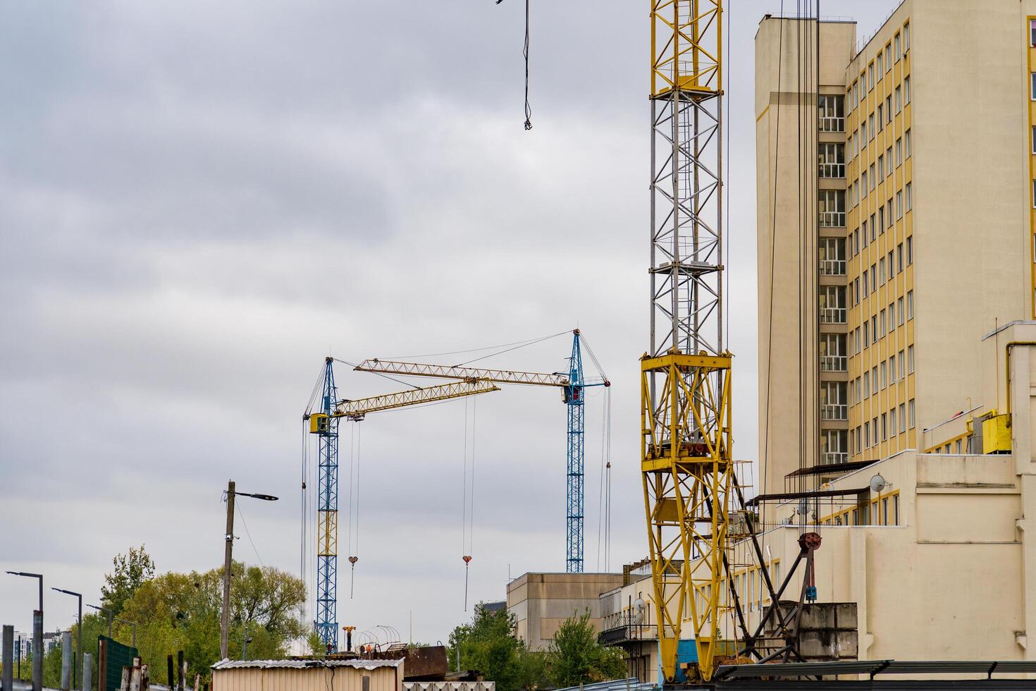Amidst a moody sky, towering cranes stand vigil over a busy urban construction site, where workers bustle about, shaping the future of the city photo