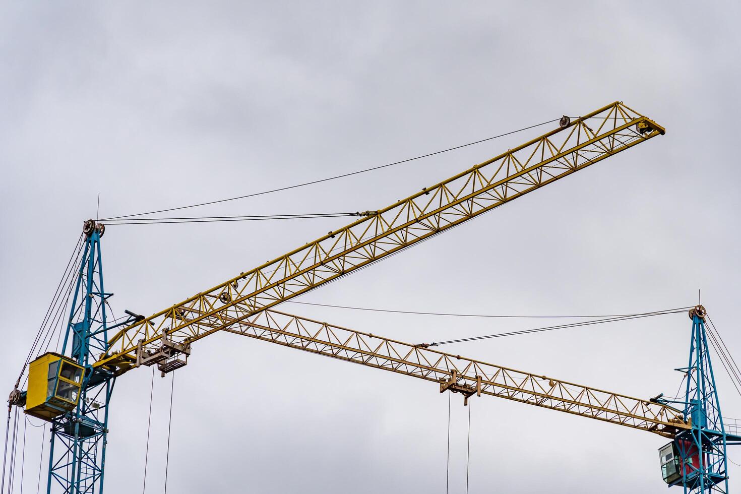Massive construction cranes stretch towards the overcast sky, showcasing their intricate structure. They are pivotal in shaping the evolving city landscape, highlighting industrial progress photo