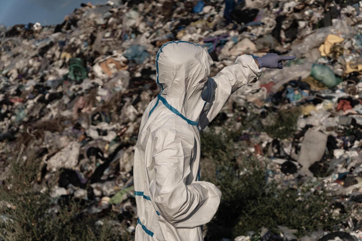 Dressed in a protective suit, a worker inspects a vast landfill, observing the layers of waste piled high and pointing out areas of concern for environmental impact photo