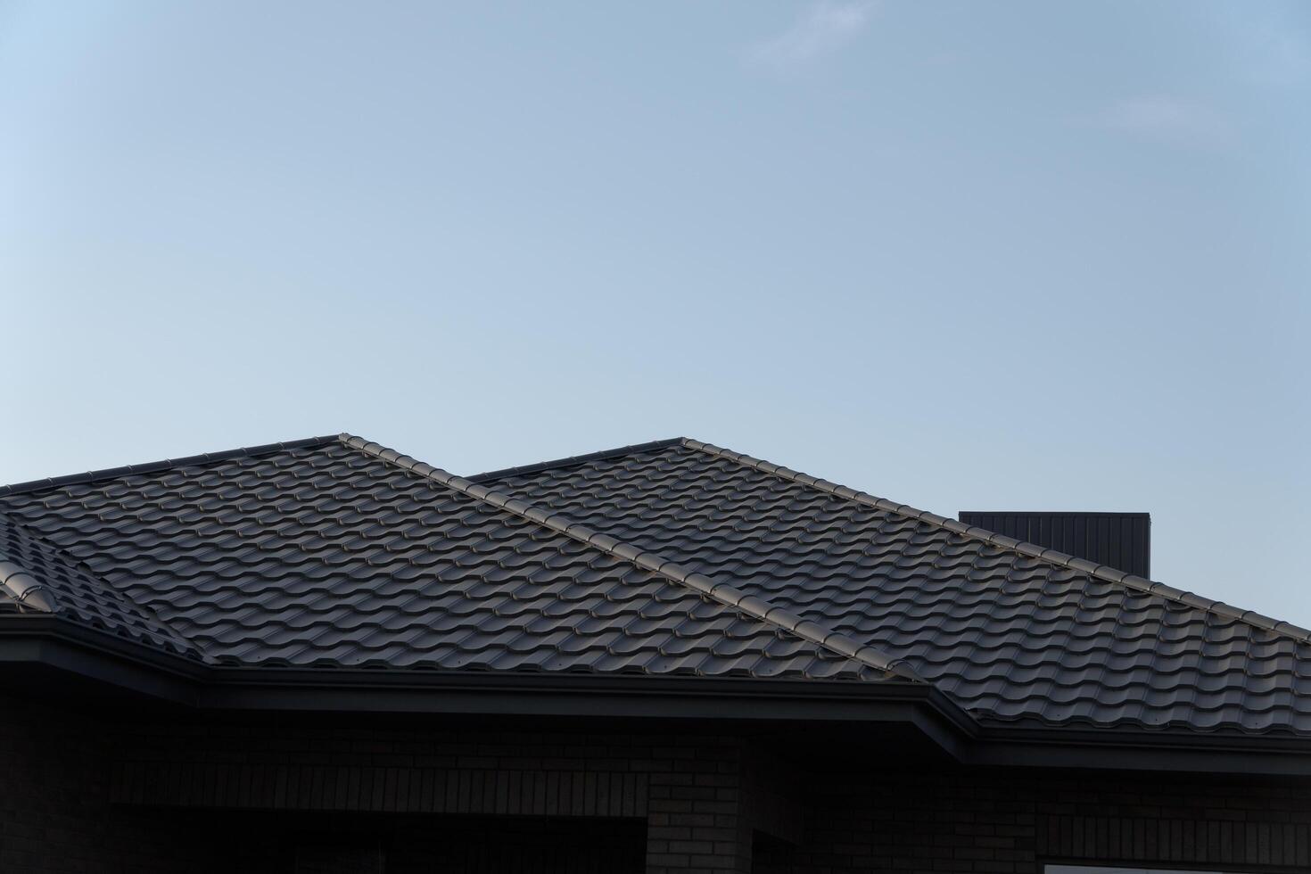 A striking view of a metal-tiled roof shines brightly against the backdrop of a clear blue sky. The architecture exudes modern charm in a peaceful suburban setting photo