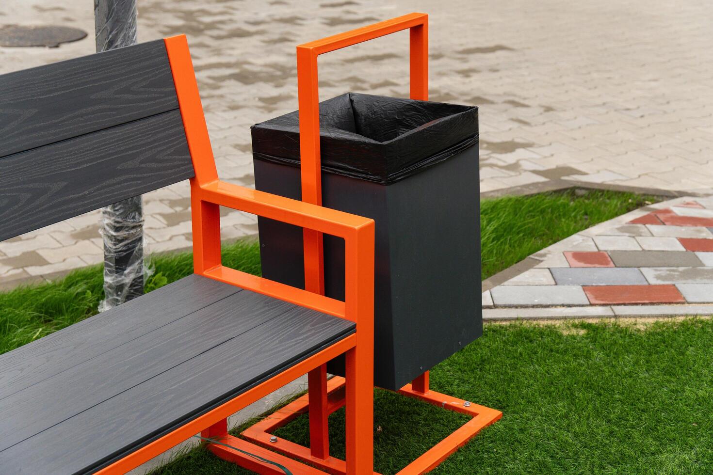 The striking orange bench designed with an attached black trash bin offers convenience for park visitors, enhancing the outdoor experience in a lively setting photo