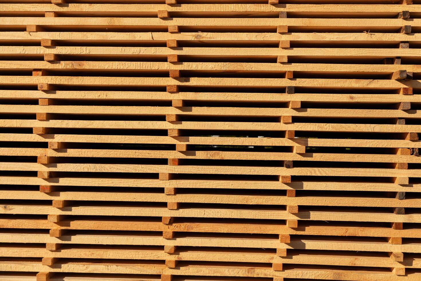 A collection of wooden pallets rests in a well-lit warehouse, their smooth surfaces reflecting the warm afternoon sunlight, creating a beautiful pattern photo