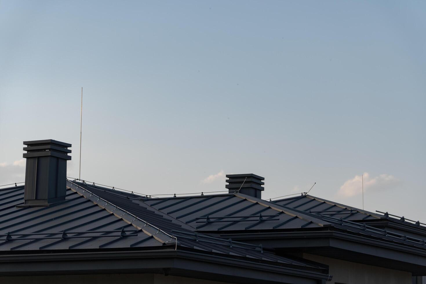 The house features a sleek, modern design with metal tile roofing. Two prominent chimneys rise from the roof, set against a bright blue sky photo