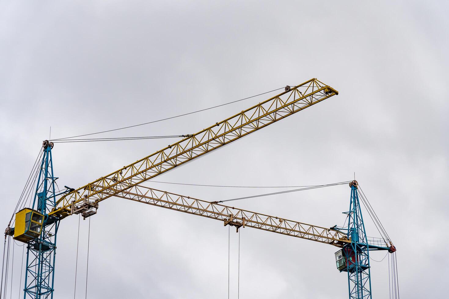 Two towering construction cranes are actively engaged in the building process of a new house, surrounded by a cloudy sky in the early morning photo