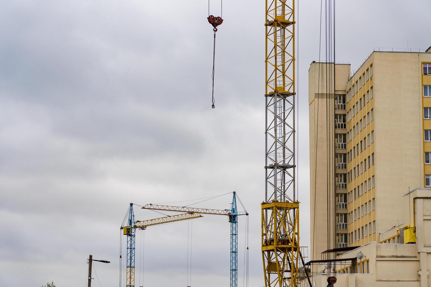 Several construction cranes are busy lifting materials at a house construction site located in a bustling urban environment during overcast weather photo