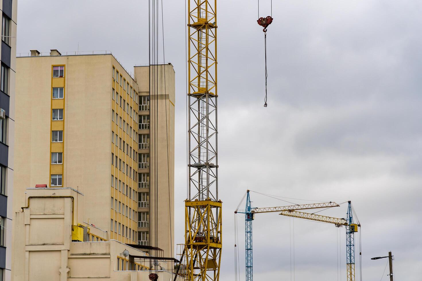 Construction cranes are actively lifting materials for a new house in an urban setting, showcasing the progress in residential development under gray skies photo