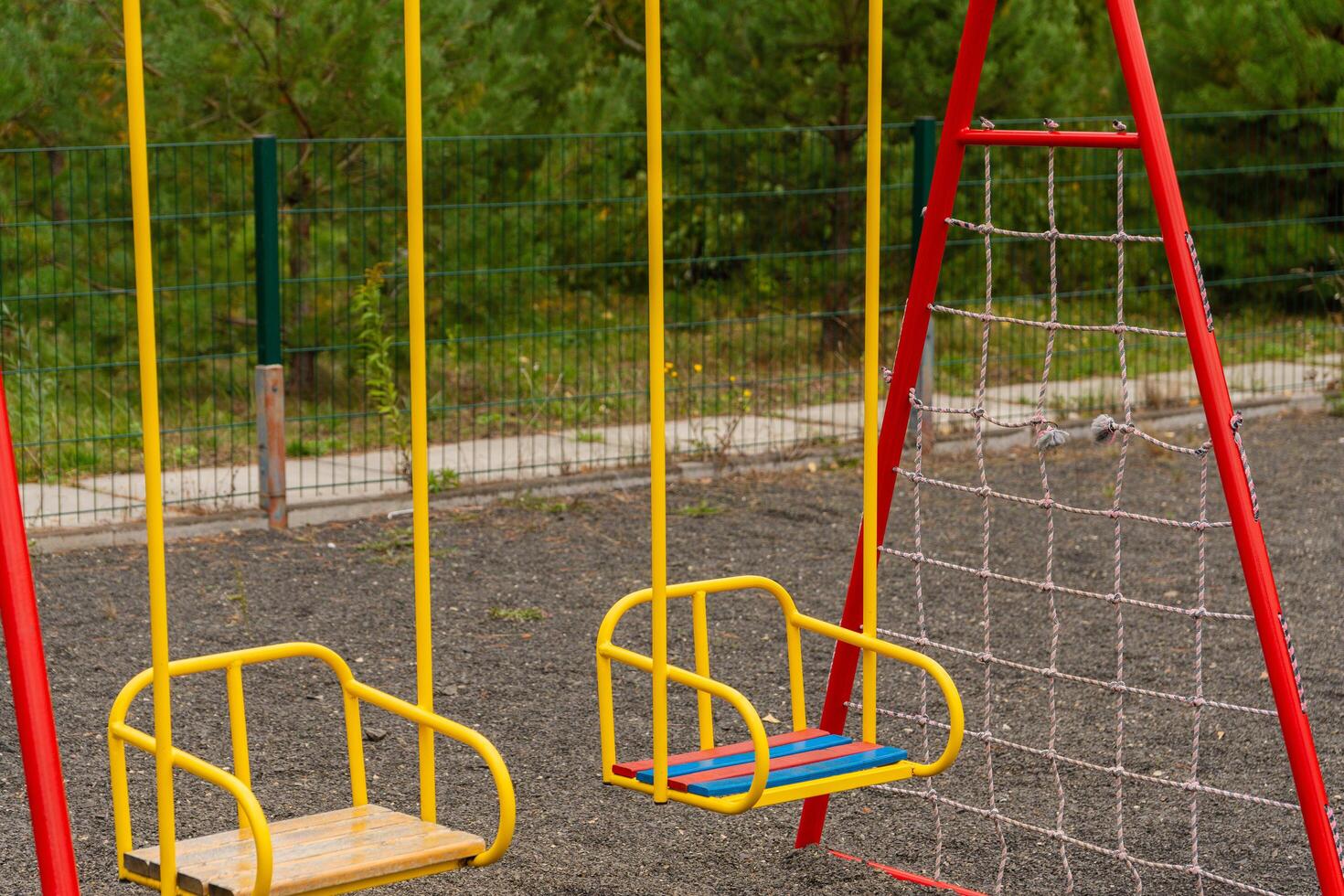 Two colorful swings stand in a public park, inviting children to enjoy swinging and playing. The vibrant setting is perfect for outdoor fun and adventure photo
