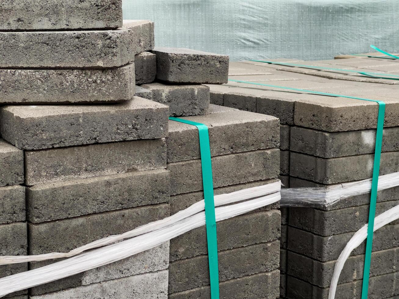 Gray brick pavers are neatly stacked and secured with straps, ready for use in paving a sidewalk on an urban street, indicating construction activity nearby photo