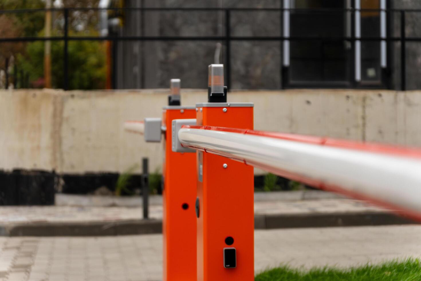 A security barrier gate is firmly closed to regulate vehicle access in a commercial area, ensuring safety and controlled entry during daylight. The design prevents unauthorized access photo