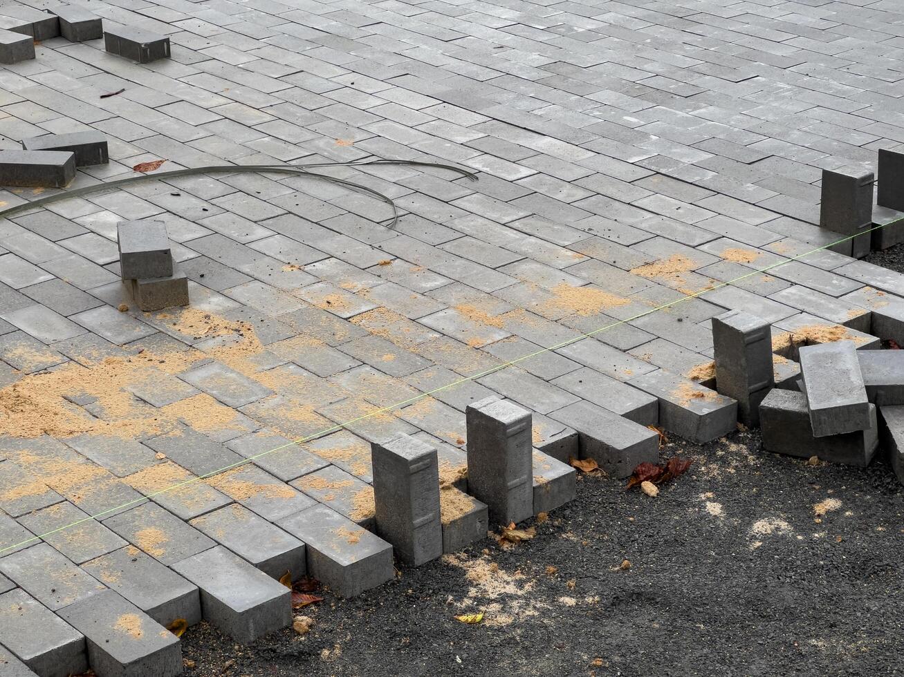 Workers are in the process of laying brick pavers to create a new sidewalk. The area shows scattered pavers and construction materials, indicating ongoing work photo