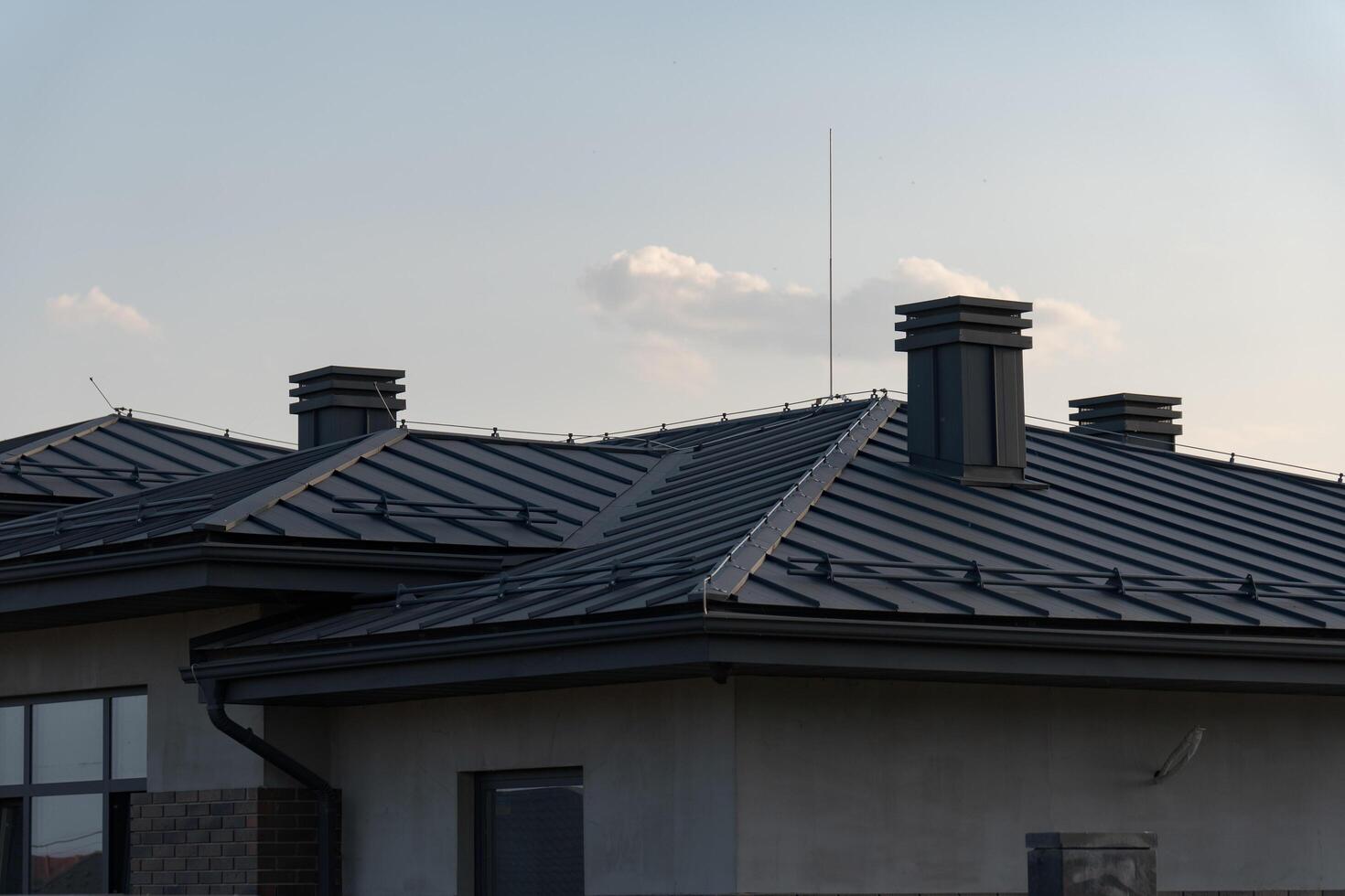 The image showcases a modern rooftop featuring slanted metal roofing and neatly arranged chimneys under a sunny sky, highlighting its construction and design elements photo