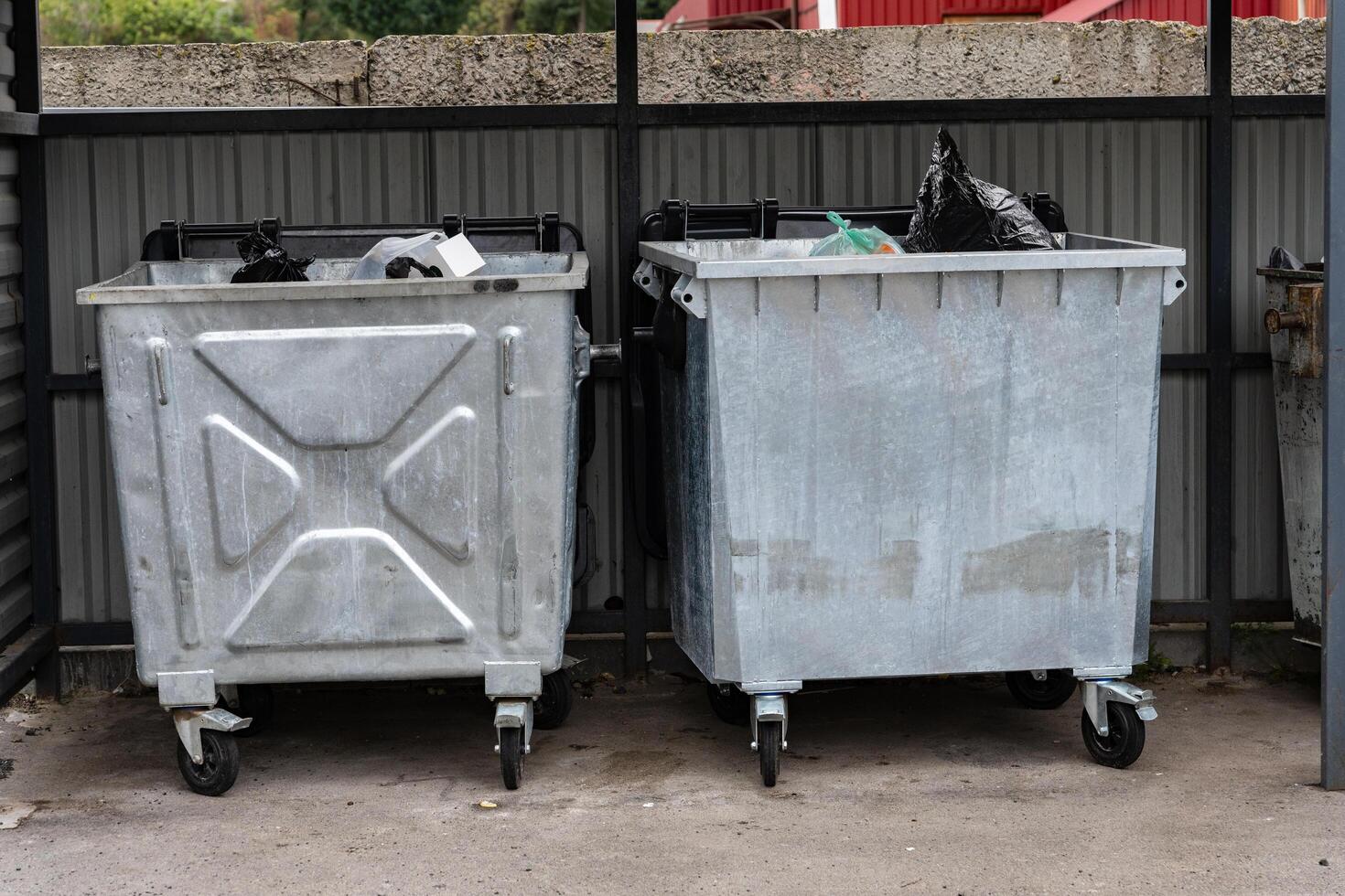 The image shows two metal garbage containers lined up together, filled with various types of waste and recycling materials in an outdoor waste disposal area photo