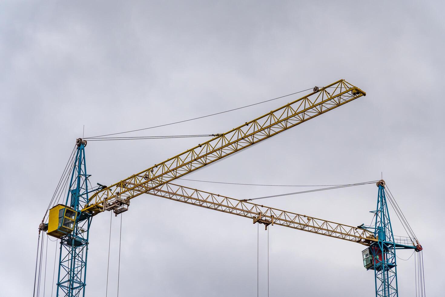 Two large construction cranes dominate the skyline, their bright yellow and blue colors contrasting against the overcast sky photo