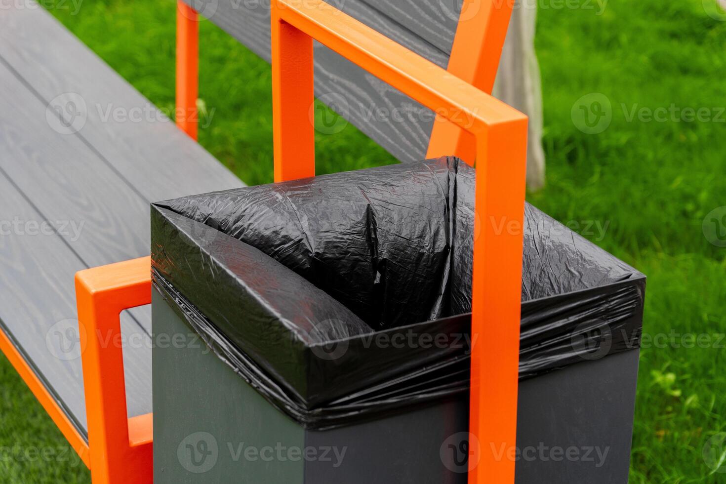 A modern bench featuring a built-in garbage container with a black liner sits on lush green grass, showcasing an aesthetic approach to waste management in public spaces photo