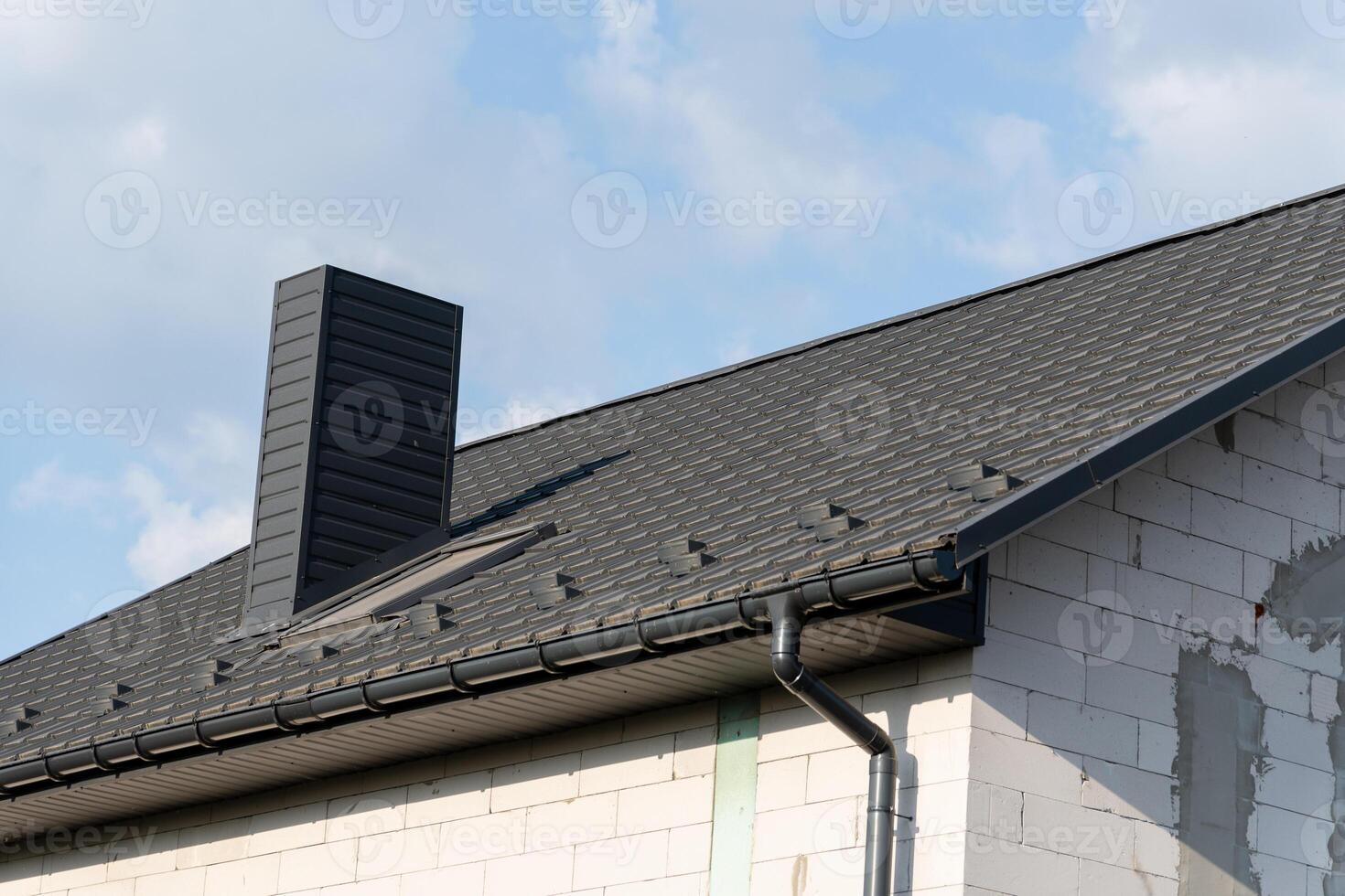 This house showcases a newly installed black metal tile roof, enhancing its modern design. A prominent chimney adds character against the clear sky photo