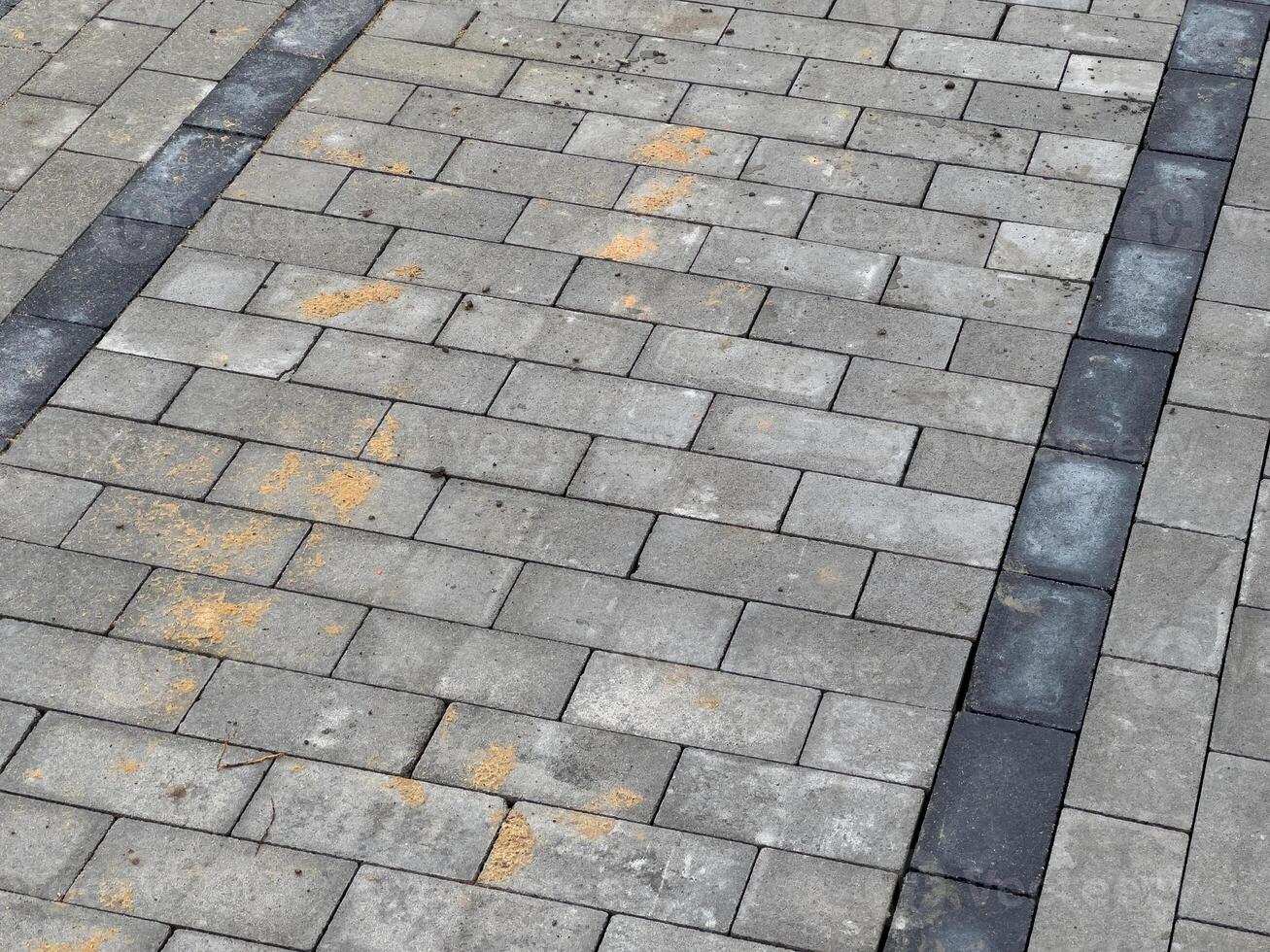 A gray brick pavement with black stripes. There is some dirt and debris on the bricks photo