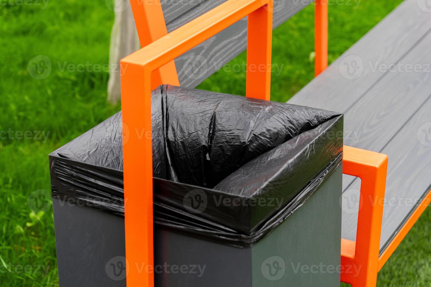 A black garbage container is attached to a park bench, showcasing a practical waste disposal solution in a well-kept grassy area, encouraging cleanliness in public spaces photo