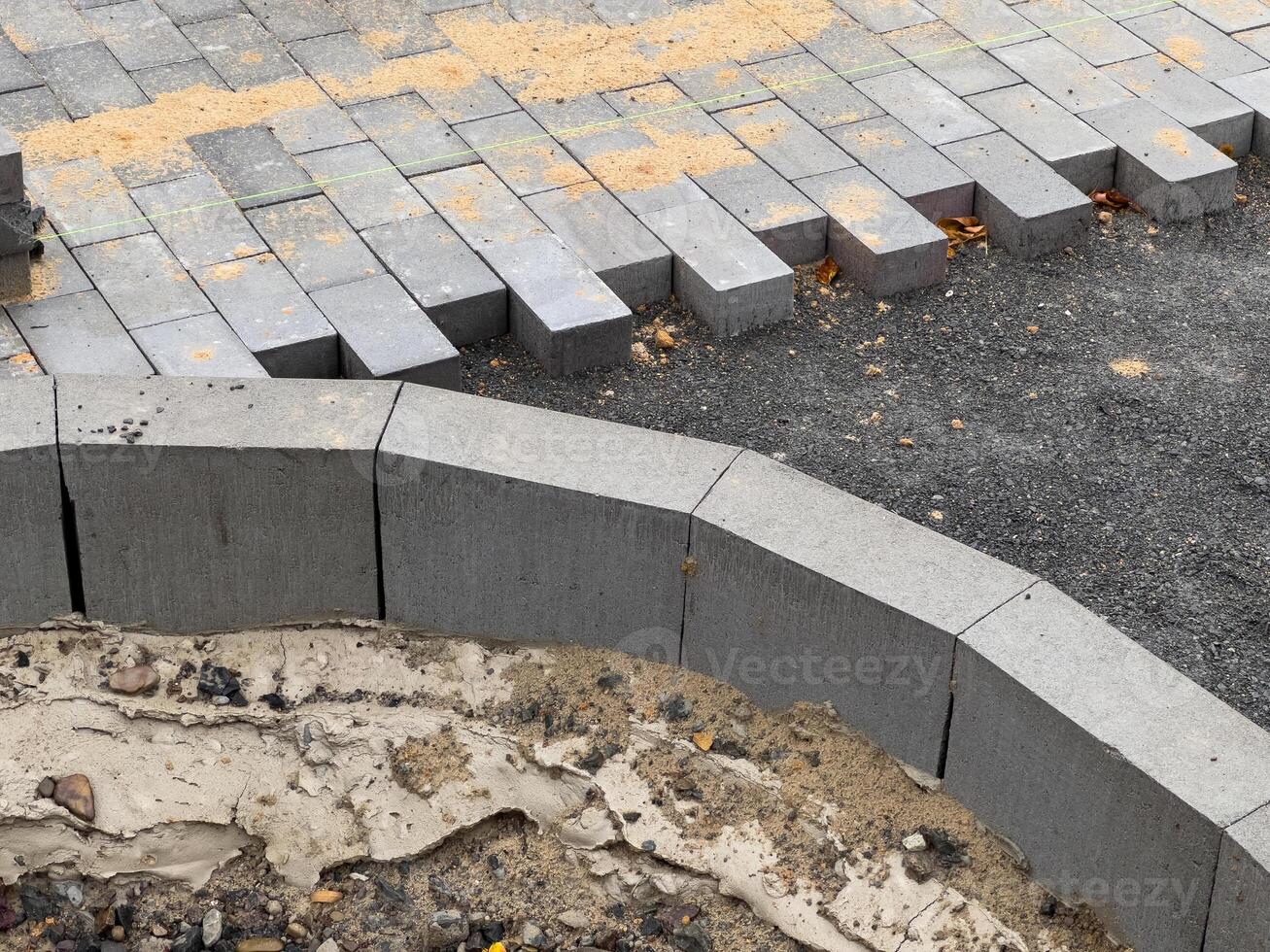 Workers are busy laying down paving stones in a construction area, where the bricks are neatly arranged, and sand is scattered nearby for leveling purposes photo