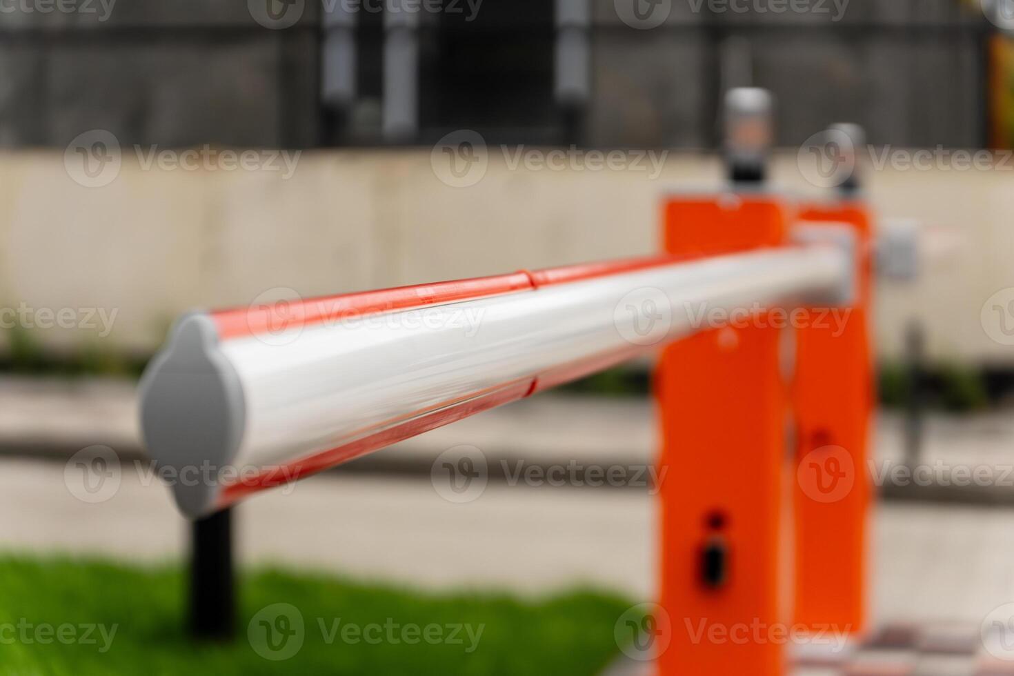 The barrier arm stretches across the entrance, poised to control vehicle access. Bright orange and silver colors catch the sunlight as vehicles approach photo
