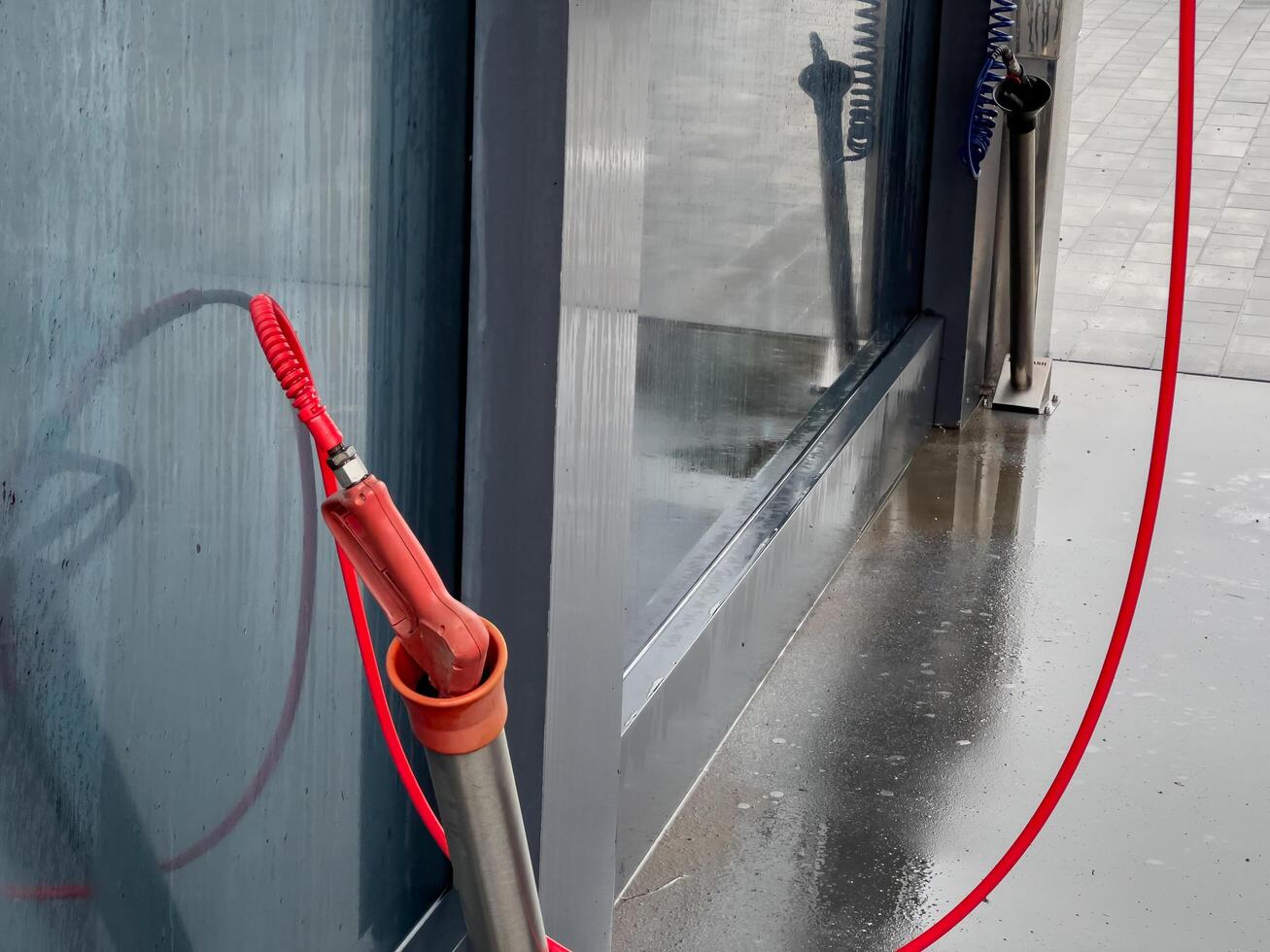 A high-pressure car washer gun stands ready for use at a self-service washing station, with droplets of water still glistening on the surface nearby photo