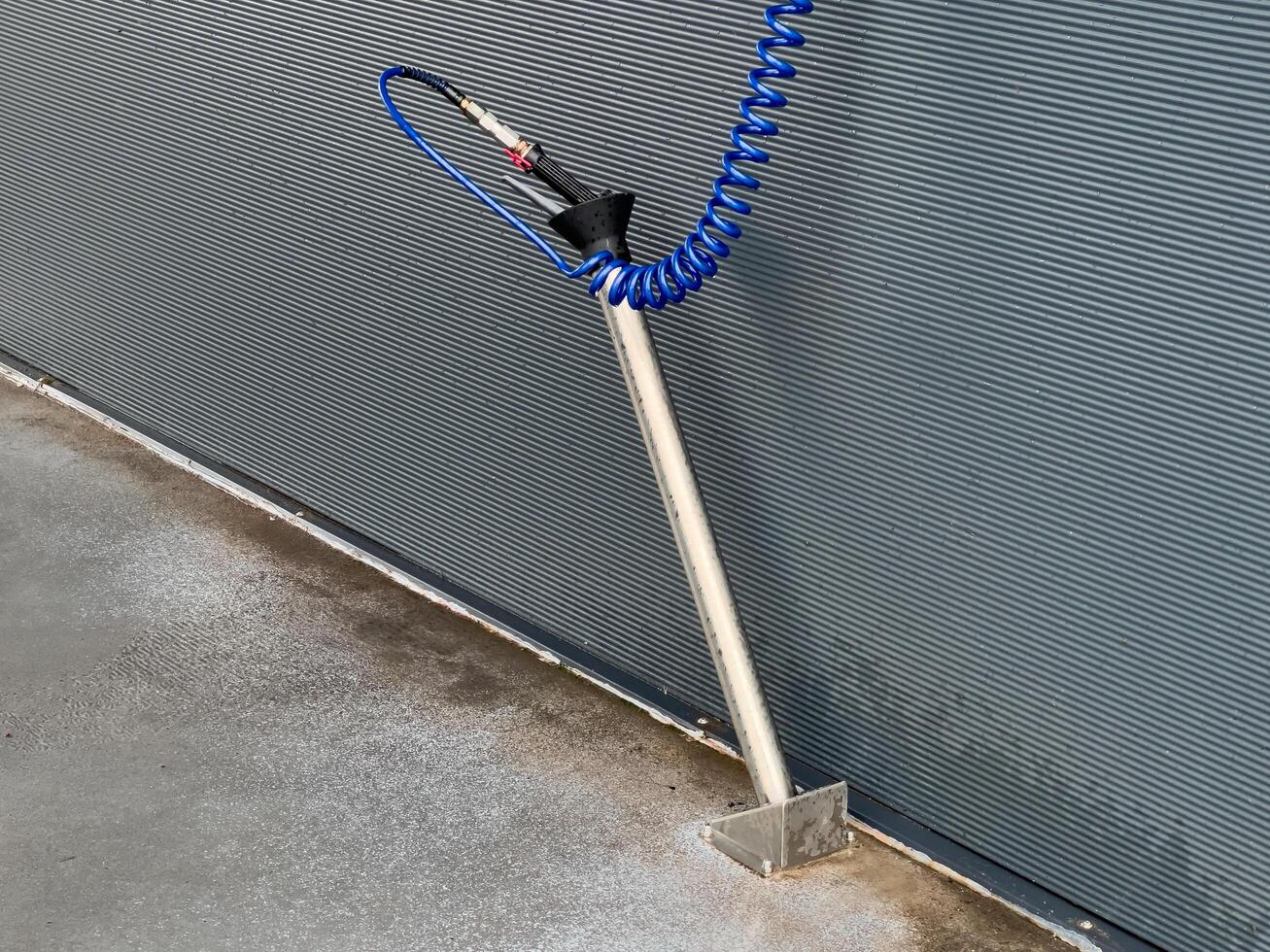 A high-pressure car washing gun is securely mounted on a stand, with a blue hose coiling to maintain readiness for effective vehicle cleaning photo
