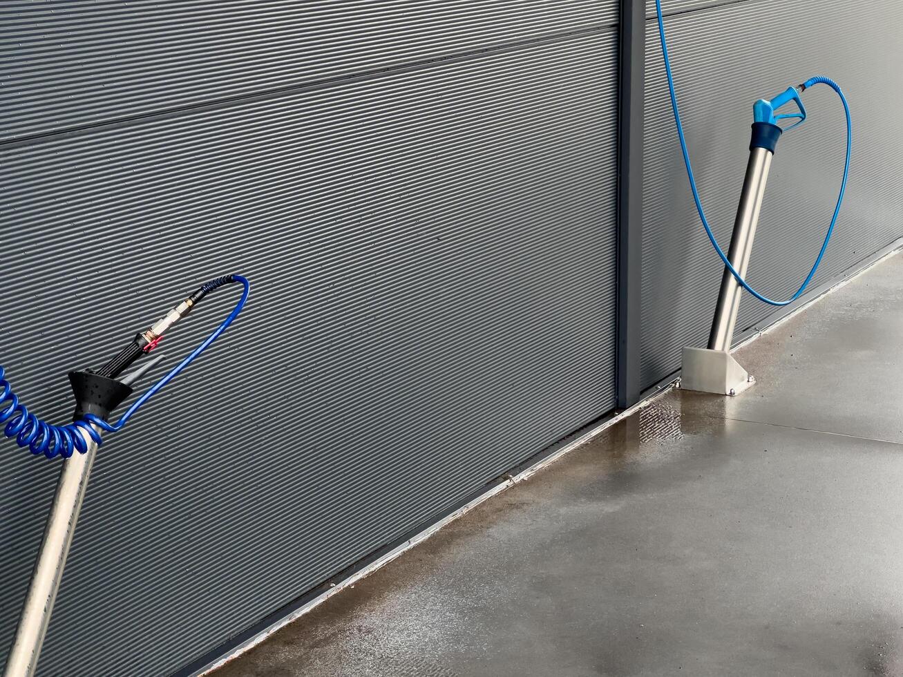 Two high-pressure car washer gun stands are positioned against a grey wall, equipped for cleaning vehicles efficiently in a well-lit automotive service space photo