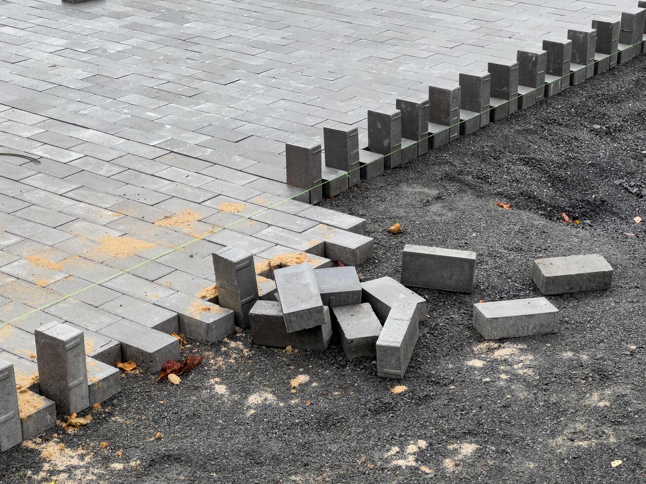 Workers are engaged in laying paving stones to create a durable pathway, with freshly placed stones visible alongside scattered bricks on the ground photo