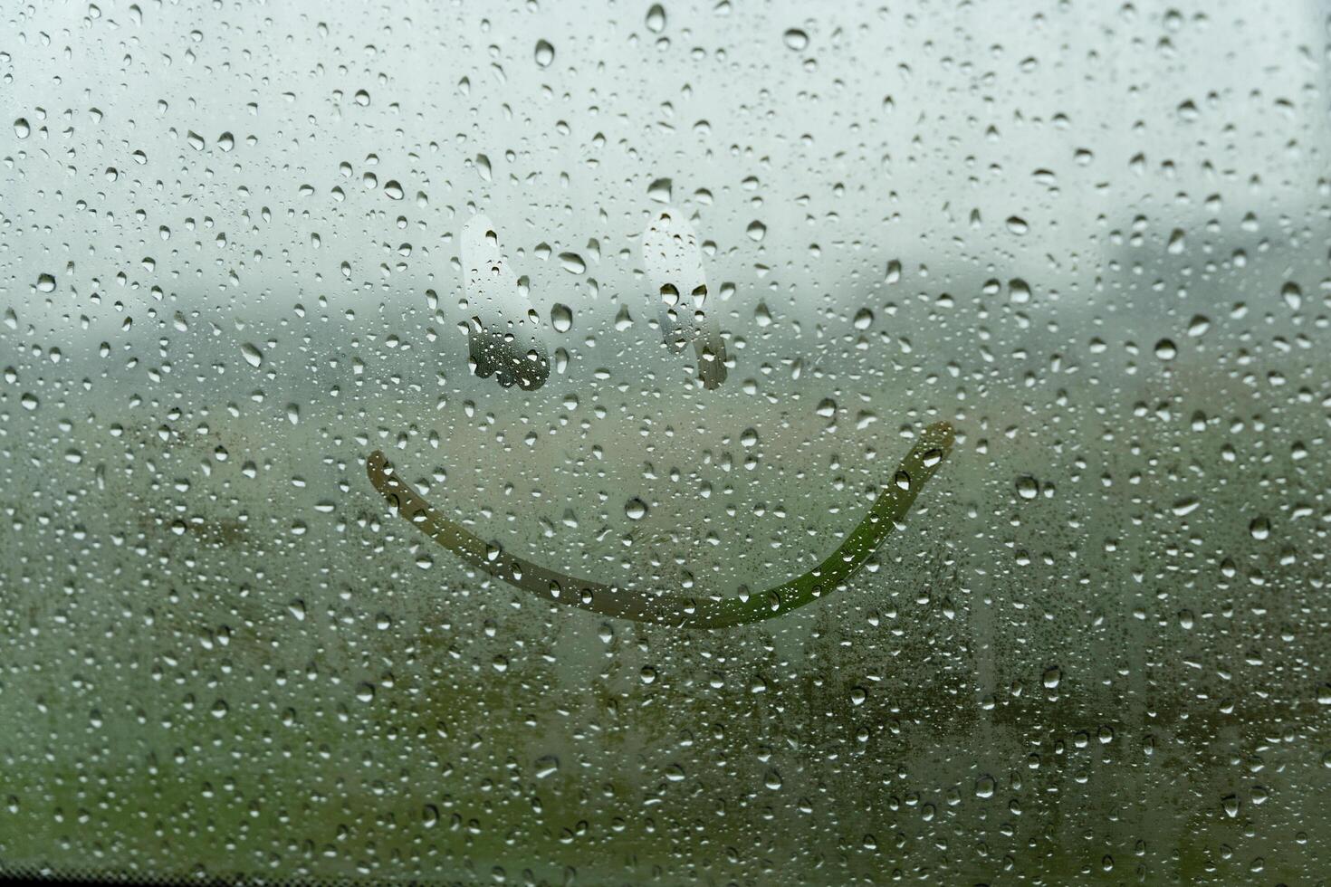 A cheerful smile is playfully etched on a fogged-up window, as rain taps against the glass, transforming an ordinary day into a moment of delight photo