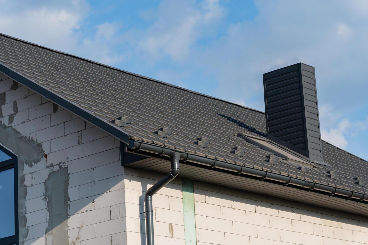 The new house features a contemporary tiled roof with a sleek design, complemented by a prominent chimney. The structure showcases a blend of modern architecture and traditional roofing photo