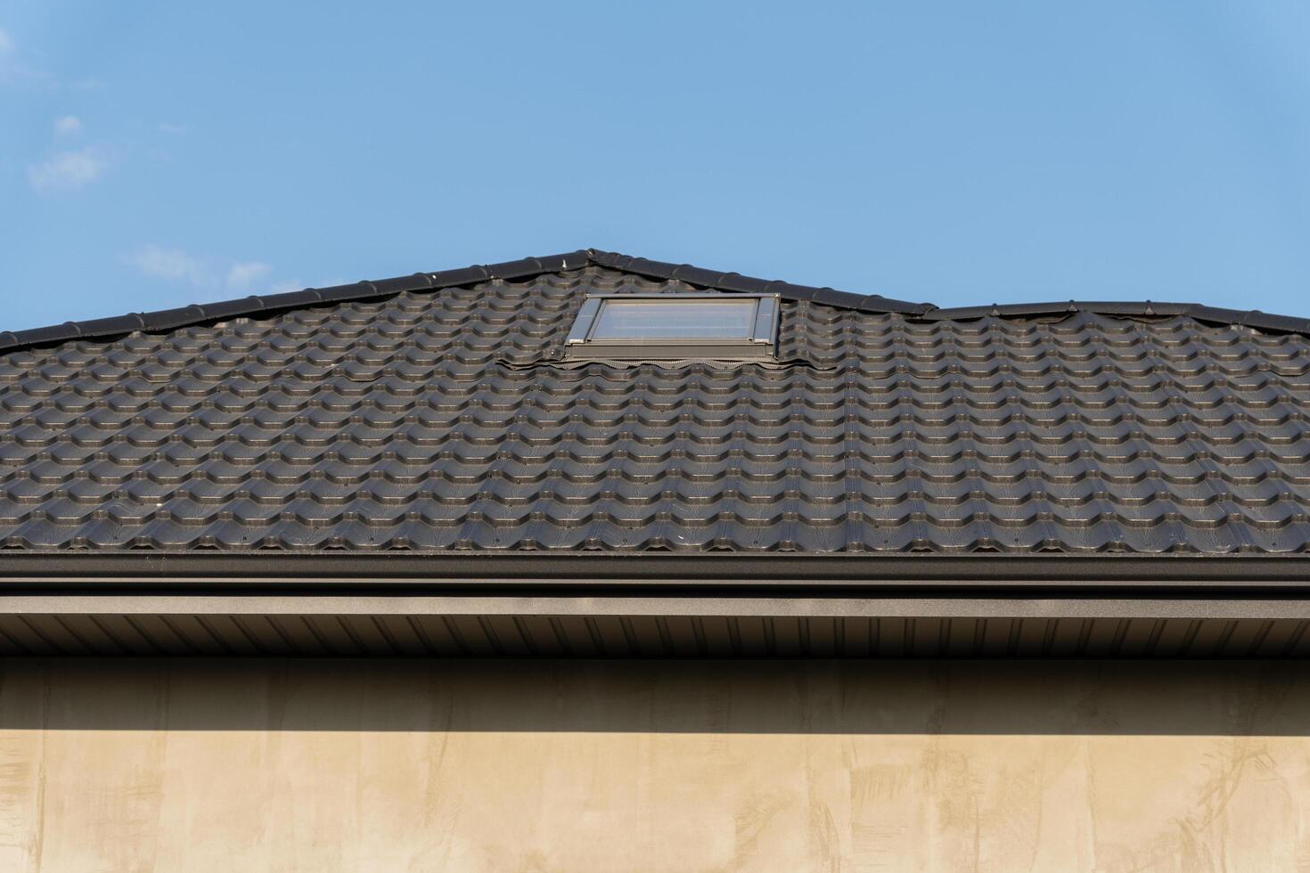 The stylish roof of a contemporary house showcases a sleek tiled design with a skylight, harmonizing with the blue sky above, highlighting modern architectural aesthetics photo