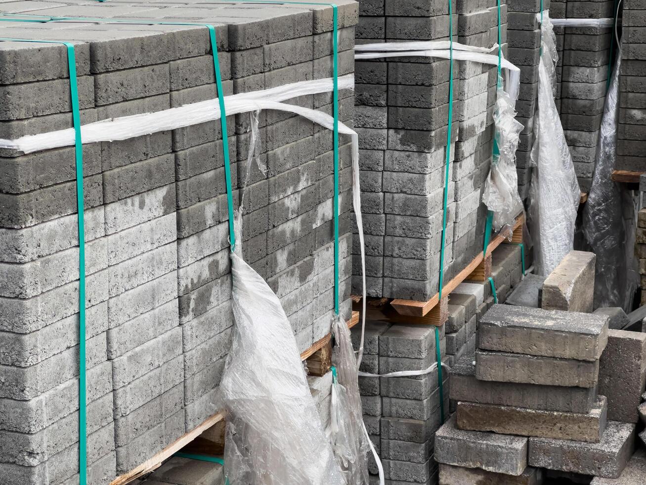 Multiple stacks of gray cobblestones are neatly arranged with plastic wrapping. They are prepared for transport, awaiting use in landscaping or road construction projects photo